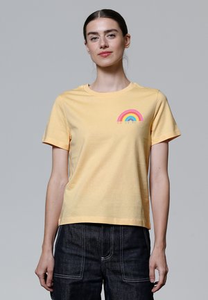 Geel katoenen T-shirt met korte mouwen, ronde halslijn en een kleine regenboogafbeelding in roze, blauw en groen gestikt op de linkerborst.