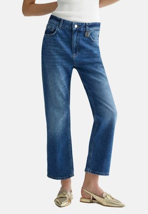 Jeans blu a vita alta con un design a gamba dritta, caratterizzati da un classico stile a cinque tasche e un leggero effetto sbiadito. Abbinati a scarpe dorate slip-on.