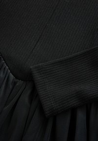 Fekete ruha bordázott felső résszel és lágy tüll szoknyával. Az anyag úgy tűnik, könnyű és puha, texturált felületű.