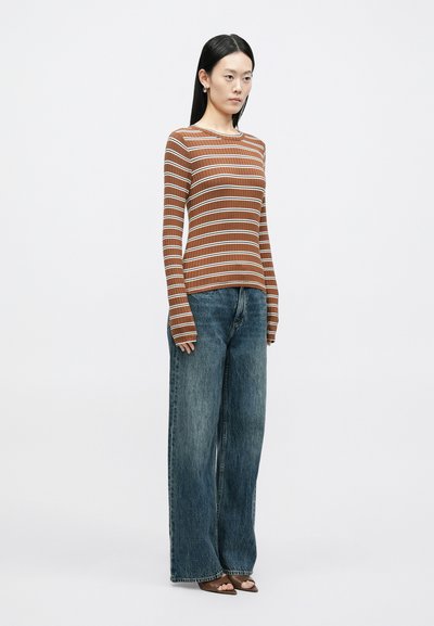 Top de manga comprida às riscas em castanho e branco, textura canelada, combinado com jeans azuis desbotados de perna larga, mostrando um ajuste descontraído e design minimalista.