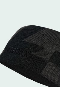 Čierny pletený čiapka s textúrovaným vzorom a diskrétnym detailom loga. Hladký materiál, zaoblený tvar a tesné priliehanie pre teplo.