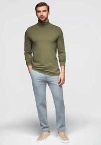 Vihreä turtleneck, istuva muotoilu, pitkät hihat; vaaleansiniset räätälöidyt housut, tekstuuri kangas; beiget lenkkarit täydentävät asua.