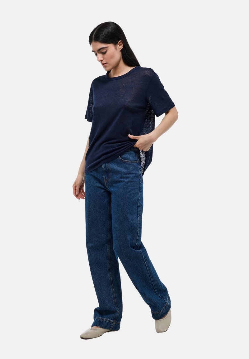 T-shirt bleu marine à manches courtes avec une coupe ample, associé à un jean bleu à taille haute et à jambes larges. Le t-shirt a une texture légère.