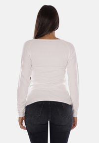 Maglione bianco a maniche lunghe, design aderente, bordo a coste, scollo rotondo, mostrato dalla parte posteriore con una texture liscia contro jeans scuri.