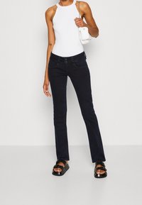 Černé rozšířené džíny s hladkým povrchem, dvěma předními kapsami a kontrastním stehem. Spárované s bílým ribbovaným bezrukávovým topem a černými sandály.