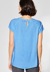 Blauwe blouse met korte mouwen, voorzien van een sleutelgatsluiting aan de achterkant, een ronde halslijn en een gladde, lichte stof met een ontspannen pasvorm.