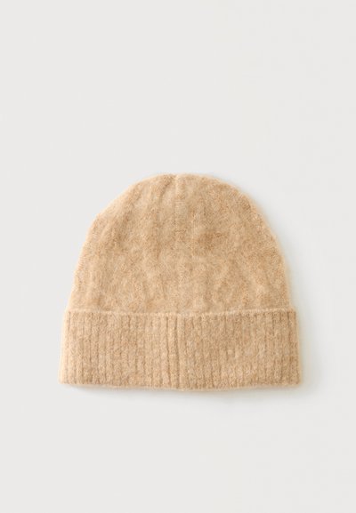 Gorro de lana beige tejido con borde acanalado doblado sobre un fondo liso y claro.