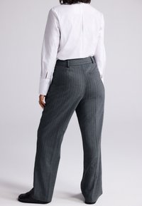 Szürke tűcsíkos nadrág, sima textúrájú anyagból, egyenes szárú kialakítással és testhezálló derékrésszel. Fehér ing látható fölötte.