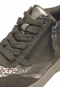 Gros plan d'une basket en daim vert foncé avec des lacets épais, une fermeture éclair latérale et un motif métallique texturé près de la semelle.