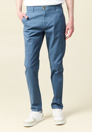 Chinos en mélange de coton bleu avec une coupe droite, dotés de poches latérales et d'une fermeture par bouton. Associés à des baskets blanches.