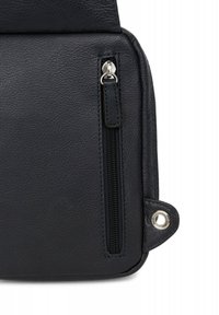 Angolo di una borsa nera in pelle con una tasca con zip, hardware della zip in argento e un accento in occhio di bue vicino alla base. Superficie liscia e texture.