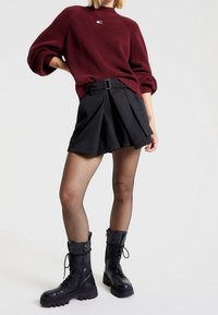 Burgundy knit sweater with a crew neck, black pleated skirt with a belt, fishnet tights, and black combat boots with a chunky sole.