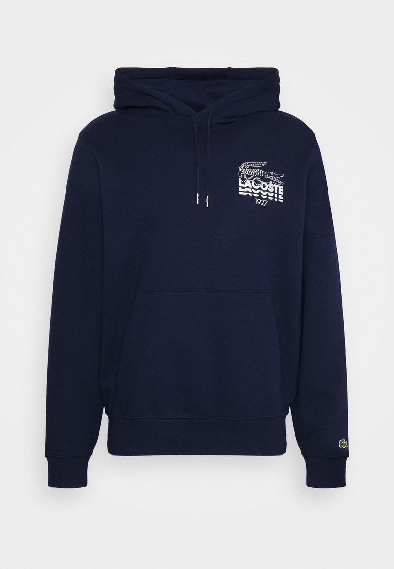 Sweat à capuche bleu marine en tissu coton, avec une poche avant et un logo Lacoste blanc avec un graphique d'alligator sur la poitrine.