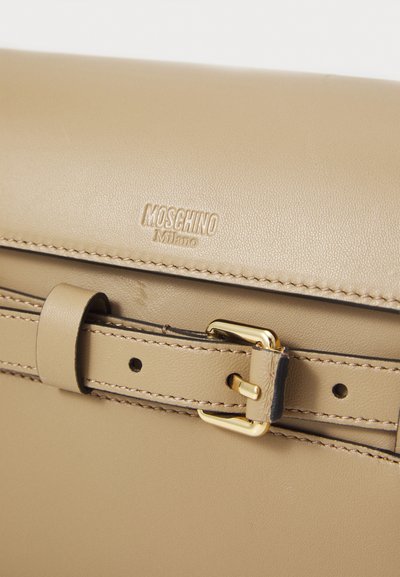 Beige leather bag featuring a gold-tone buckle, stitching details, and embossed "Moschino Milano" logo on the front flap.