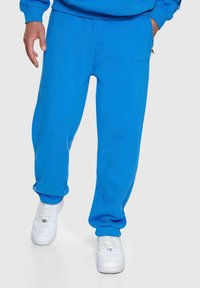 Blaue Sweatpants aus einem glatten Baumwollgemisch, mit einem elastischen Bund und Bündchen, kombiniert mit weißen Sneakers. Einfaches Design, keine sichtbaren Muster.