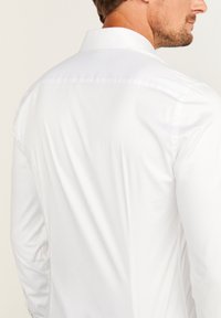 Witte lange mouwen shirt met een standaardkraag, gladde stof en subtiele textuur, met zijnaadstiksels en zonder zichtbare patronen of grafische elementen.
