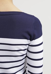 Marinblå och vit randig långärmad topp med rund halsringning, ribbad textur och figursydd silhuett som visar detaljer på axlar och ärmar.