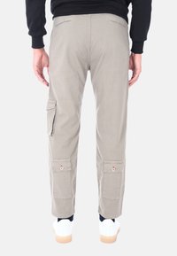 Pantaloni cargo grigio chiaro con tasche laterali e dettagli con bottoni, realizzati in un tessuto resistente, abbinati a sneakers bianche su uno sfondo semplice.