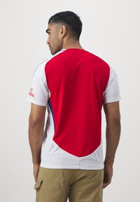 Maillot rouge et blanc à manches courtes avec un motif texturé, présentant des accents bleus sur les côtés et un logo sur la manche gauche.