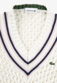 Πλεκτό εκρού πουλόβερ με V-λαιμόκοψη, διακοσμημένο με ριγέ μανσέτες σε χρώματα ναυτικό μπλε, ροζ και πράσινο, και μικρό πράσινο λογότυπο κροκόδειλου στο στήθος.