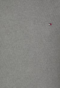 Tissu gris texturé avec un motif subtil. Présente un petit emblème aux rayures rouges, blanches et bleues dans le coin.