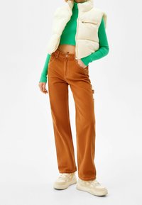 White puffer vest, green ribbed crop top, and brown wide-leg pants. Sneakers with light-colored accents. Smooth textures and casual design.
