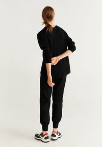 Black sweater and jogger set, featuring a relaxed fit. The material appears soft with ribbed cuffs. Shoes have a white sole with black and red accents.