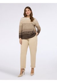 Stickad tröja med gradientnyanser av beige och brunt, kombinerad med beiga byxor och nude högklackade skor. Enkel, avslappnad design.