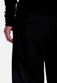 Pantalon noir à fines rayures avec une poche plate à l'arrière et un tissu lisse et texturé, associé à un haut noir ajusté à manches longues.