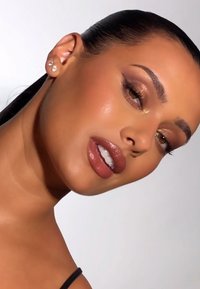 Frau mit glatter Haut und hellbraunem Lippenstift; trägt Diamantstecker, mit glattem, glänzendem Haar, das nach hinten gestylt ist.