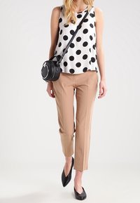 Top sans manches à pois blanc et noir, associé à un pantalon beige à jambe fuselée. Accessoirisé avec un petit sac bandoulière noir et des ballerines noires.