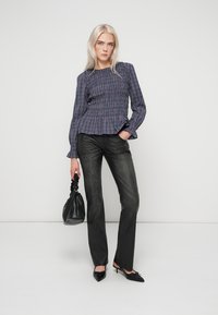 Kék és fehér kockás blúz smockolt részletekkel, sötét szürke egyenes szárú farmernadrággal párosítva. Kiegészítők között szerepel egy fekete kézitáska és hegyes orrú magassarkú cipő.