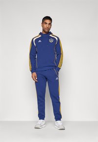 Blue athletic tracksuit featuring a hooded top with yellow accents and white stripes, paired with matching blue pants and white sneakers.