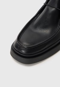 Svart lädersko med rund tå, sydda detaljer och en tjock gummisula. Slät yta och minimalistiska designelement.