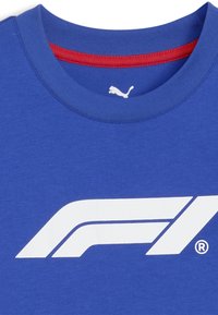 Modrá bavlněná trička s výrazným bílým logem F1. Kulatý výstřih s červeným lemem a krátkými rukávy. Měkká textilie s pohodlným střihem.
