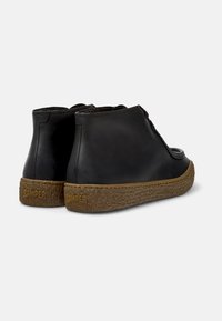 Schwarze Lederstiefeletten mit einer strukturierten braunen Gummisohle und runder Zehenform, versehen mit dezenten Nähdetails und einem Camper-Logo an der Ferse.