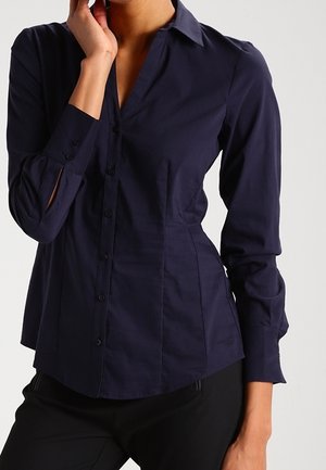 Navy blue button-up shirt with long sleeves, a collar, and fitted design; features soft texture and subtle side seam detailing.