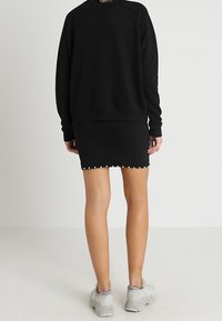 Schwarzer Pullover mit lockerem Sitz und Raglanärmeln, kombiniert mit einem enganliegenden schwarzen Rock, der entlang des Saums mit kleinen weißen Nieten verziert ist.