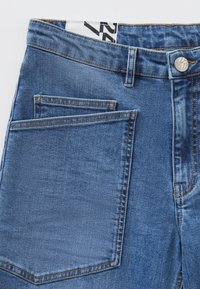 Blå denimjeans med hög midja, metallknappslå och en framträdande framficka med en ren sömdesign.
