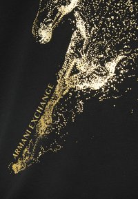 Gold dotted design of a runner’s leg and foot with "ARMANI EXCHANGE" text on black fabric background.