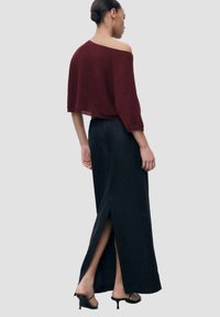 Bordový pletený top bez ramínek v kombinaci s dlouhou černou sukní s vysokým rozparkem. Tento outfit zdůrazňuje spojení ležérní elegance.