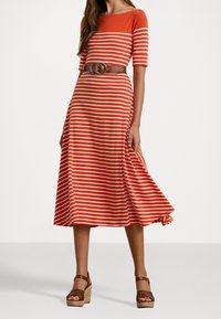 Punainen ja valkoinen raitamekko, jossa on lyhyet hihat, istuva yläosa ja levenevä hame, jota korostaa ruskea vyö, jossa on pyöreä solki.