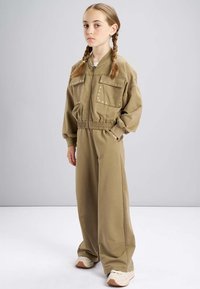 Khaki twee-delige outfit met een rits bomberjack, twee voorzakken en wijde broekspijpen. Gemaakt van zacht, soepel materiaal met een comfortabele pasvorm.