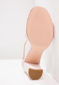 Vaaleanpunainen nahkakengät, joissa on sileä pinta, säädettävä hihna ja kuvioitu kumipohja. Varressa on lohkokorkodesign.