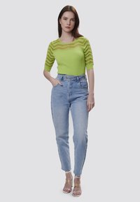 Helles grünes ribbed Strickoberteil mit transparenten gestreiften Akzenten, kombiniert mit hochgeschnittenen hellblauen Jeans und transparenten, hochhackigen Sandalen.