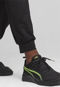 Svarta sportskor i mesh och syntetiska material. Har gröna accentlinjer, texturerad yta och rundad tå. Snörningsdesign.