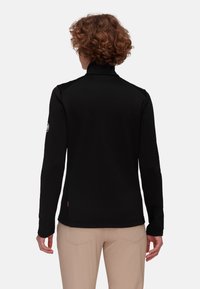 Giacca nera a maniche lunghe con colletto alto, texture liscia e design aderente. Presenta una toppa logo sulla manica e un accento arancione sull'orlo.