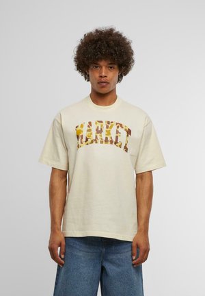 Cremefarvet bomulds t-shirt med korte ærmer og rund hals, prydet med et camouflagemønster af "MARKET" grafik i nuancer af brun og gul.