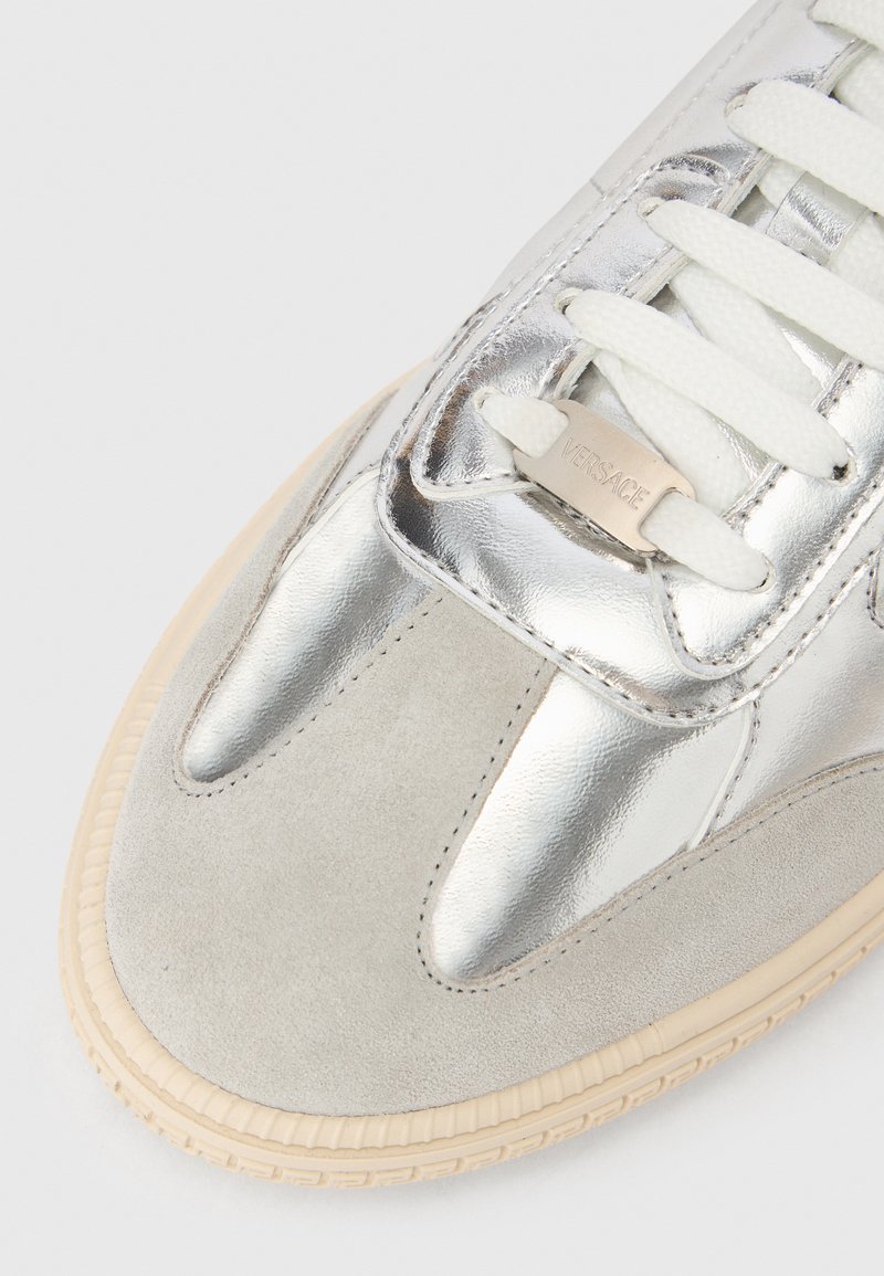 Sneaker metallizzato argento con dettagli in pelle scamosciata, laccetti crema, design elegante e suola texturizzata per presa e durata.