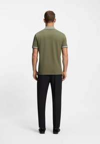 Polo de color verde oliva con un cuello texturizado y estampado, mangas cortas y detalles en gris, combinado con pantalones y zapatos negros.